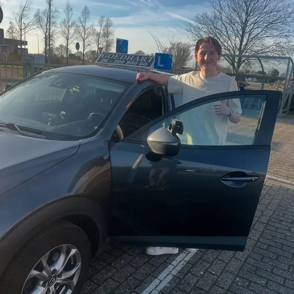 Geslaagde leerling Jesse bij de grijze lesauto van Autorijschool Goedhart